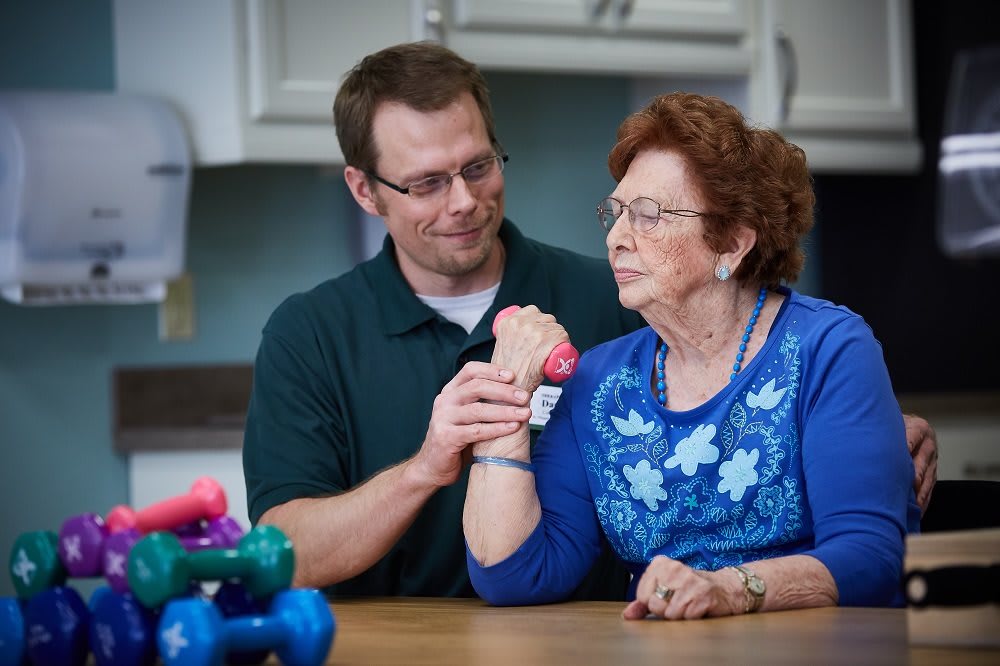 A healthcare professional assists an elderly woman with physical therapy exercises.