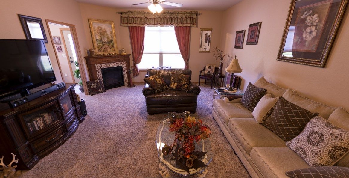A cozy living room with a sofa, armchair, and a fireplace, featuring warm decor and curtains.