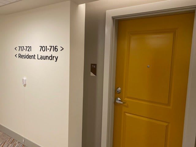 A hallway in a building with a yellow door and a sign indicating room numbers and student laundry.
