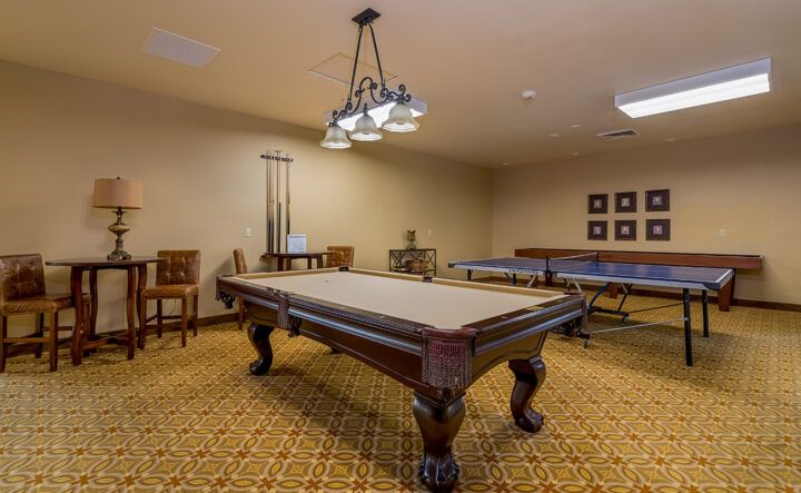 A well-furnished billiards room featuring a central pool table under stylish lighting.