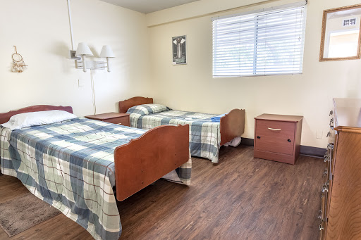 A simple hospital room featuring two twin beds with plaid blankets and a window.