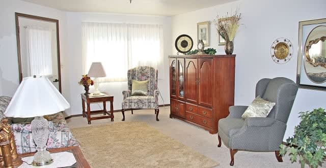A cozy living room with traditional decor, featuring a patterned armchair, wooden cabinet, and soft lighting.