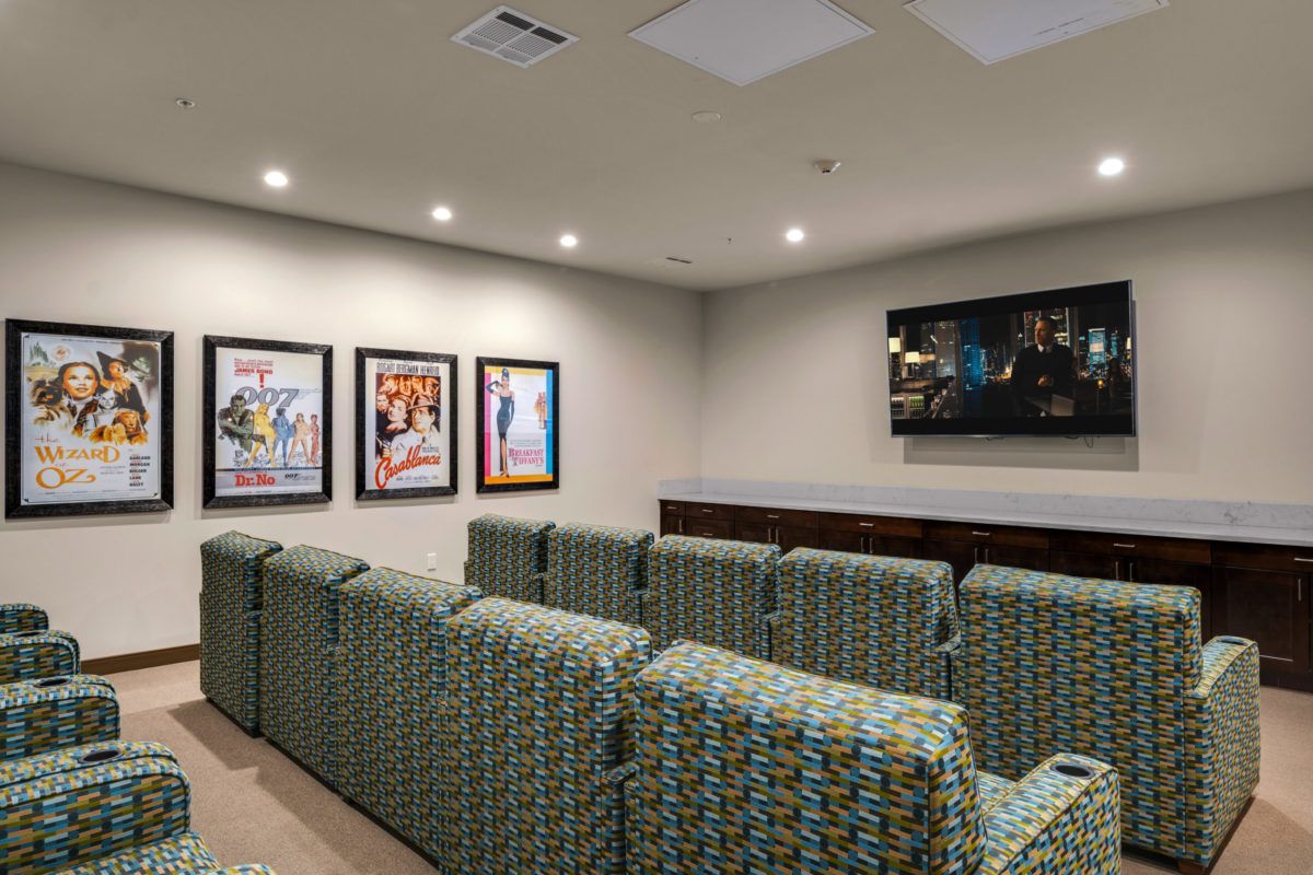 A cozy home theater room with patterned seating, movie posters on the wall, and a large screen for viewing.