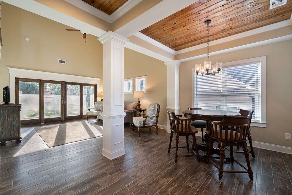 A well-lit dining room with a wooden floor and coffered ceiling, featuring elegant furniture and a chandelier.