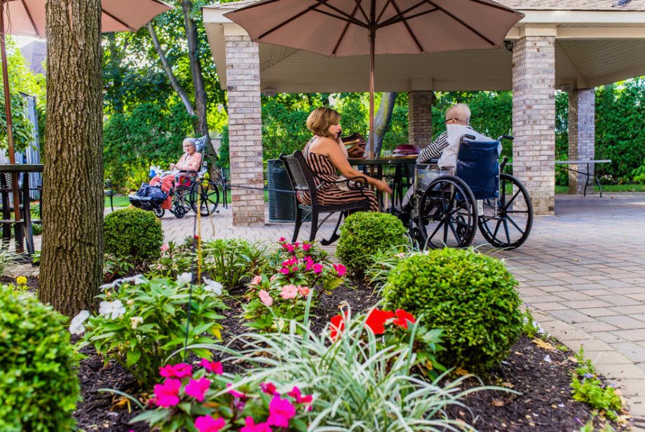 Seniors enjoy a peaceful afternoon in a garden patio setting, surrounded by colorful flowers.