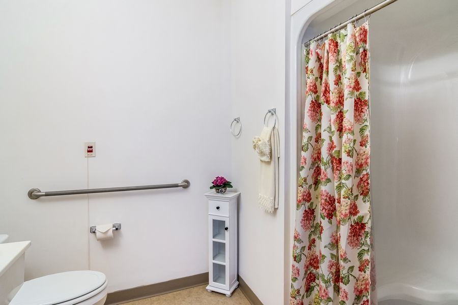 A clean bathroom with a floral shower curtain and safety grab bar.