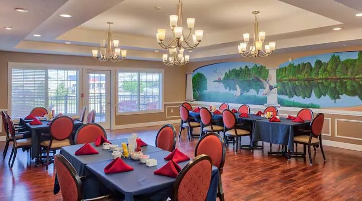 A well-decorated dining room with elegant chandeliers, mural on the wall, and tables set with red napkins.