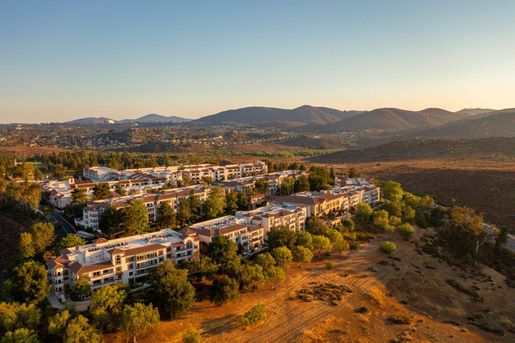 Aerial view of a residential area nestled among trees with mountains in the background during sunset.