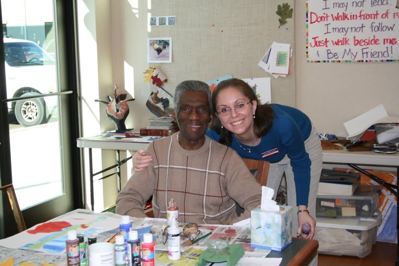 Two people smiling and embracing in a room with art supplies.