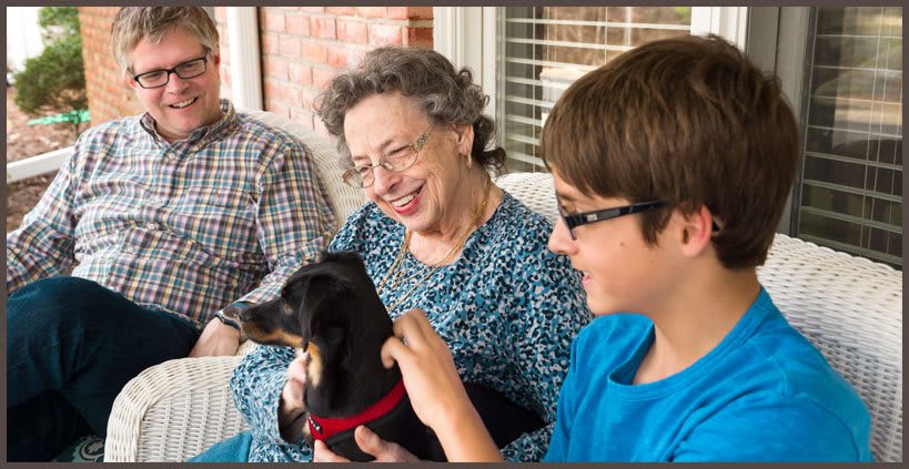 A family spending time together outdoors, with an elderly woman and a young boy smiling while petting a dog.