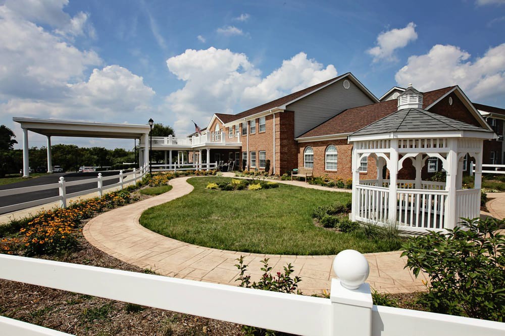 A scenic view of a landscaped garden with a brick building, white gazebo, and pathway under a partly cloudy sky.