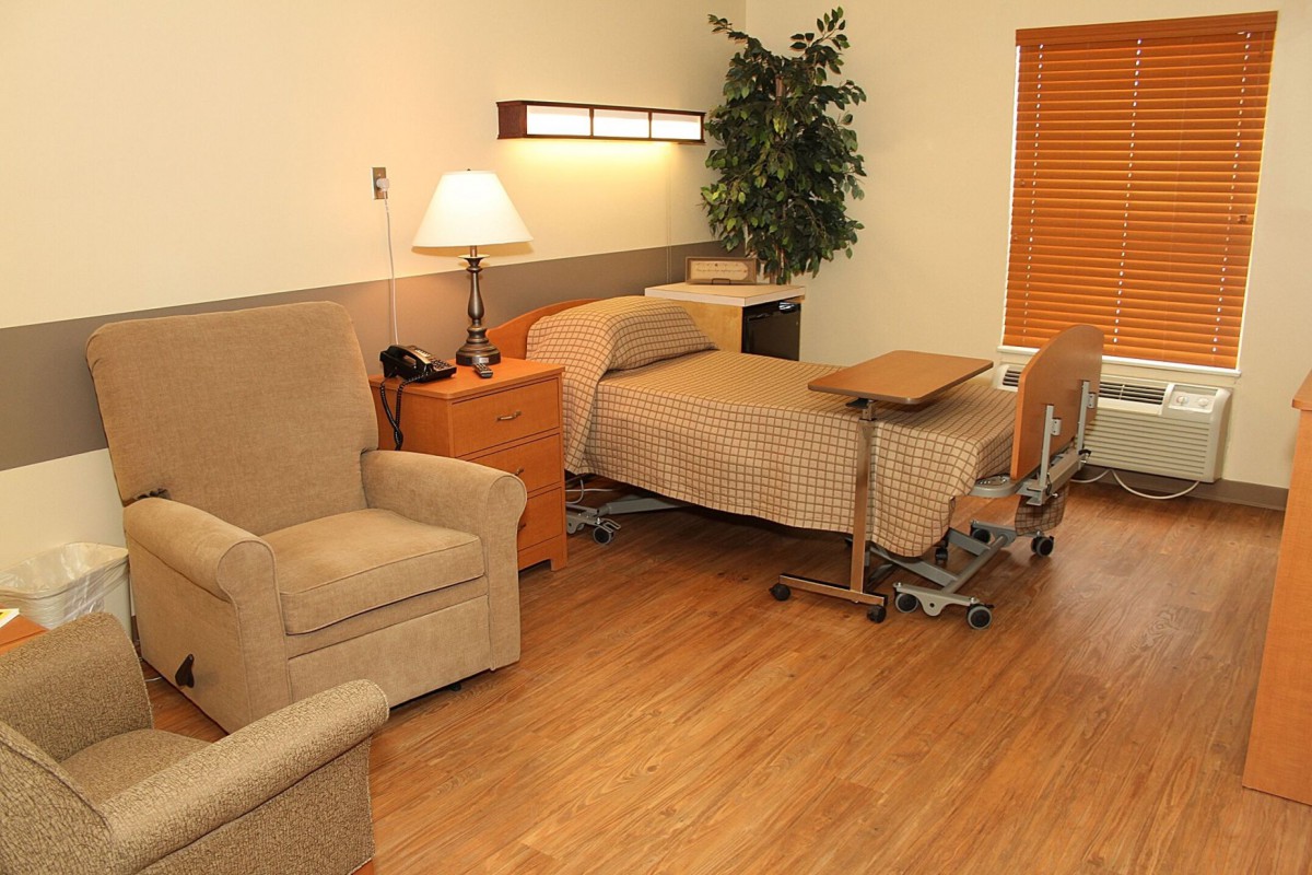 A well-furnished hospital room featuring a bed, chair, and bedside furniture.