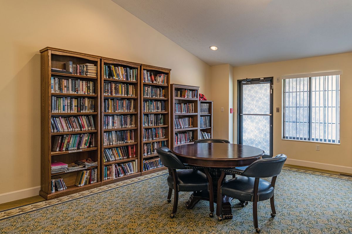 A cozy library corner with bookshelves and a round table surrounded by chairs.