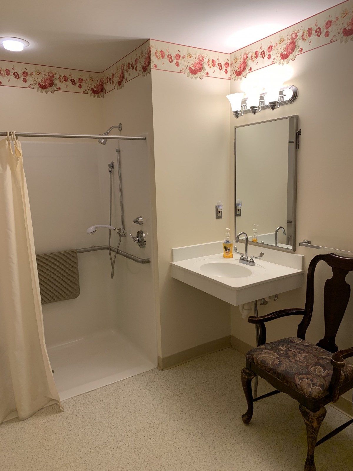 An accessible bathroom with a walk-in shower, sink, and chair.