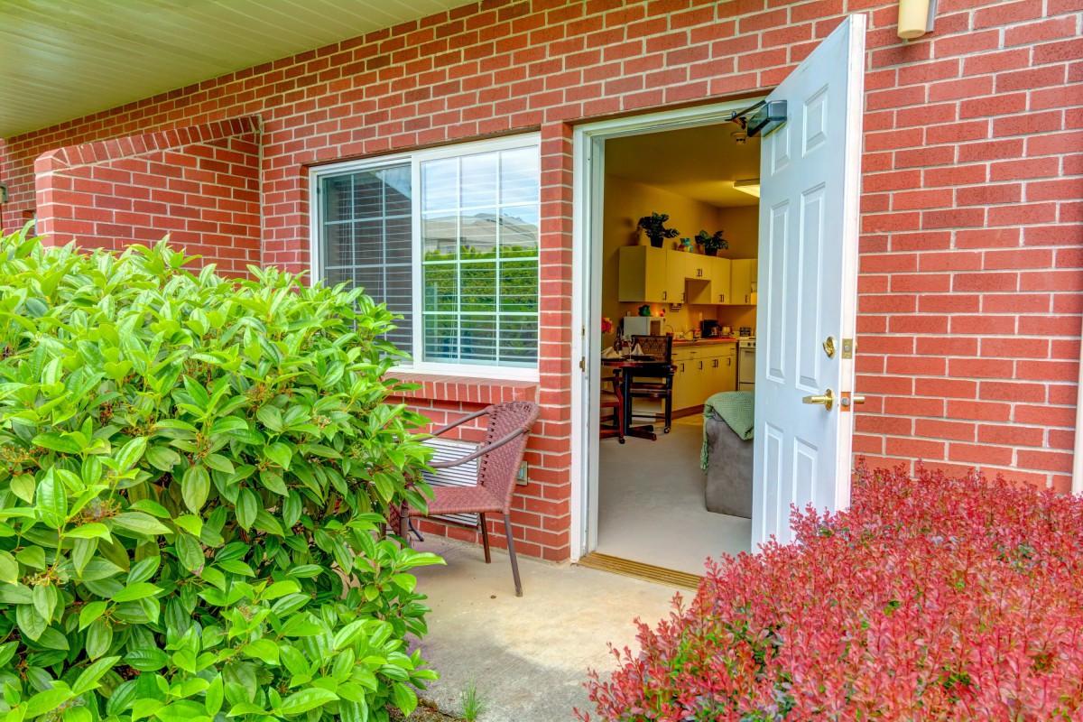 A welcoming open door leads into a cozy home, bordered by lush greenery and patio furniture.