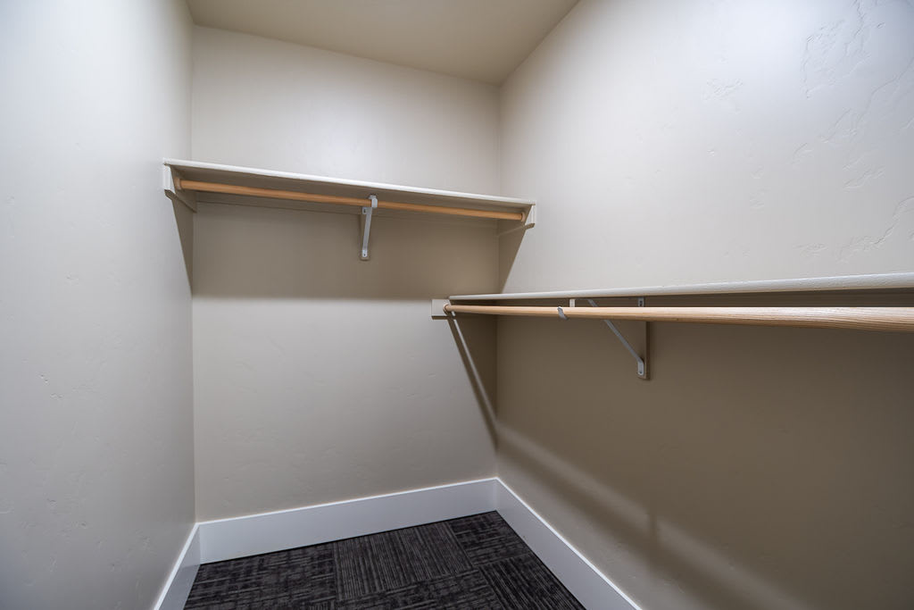 An empty walk-in closet featuring wooden shelves and hanging rods.
