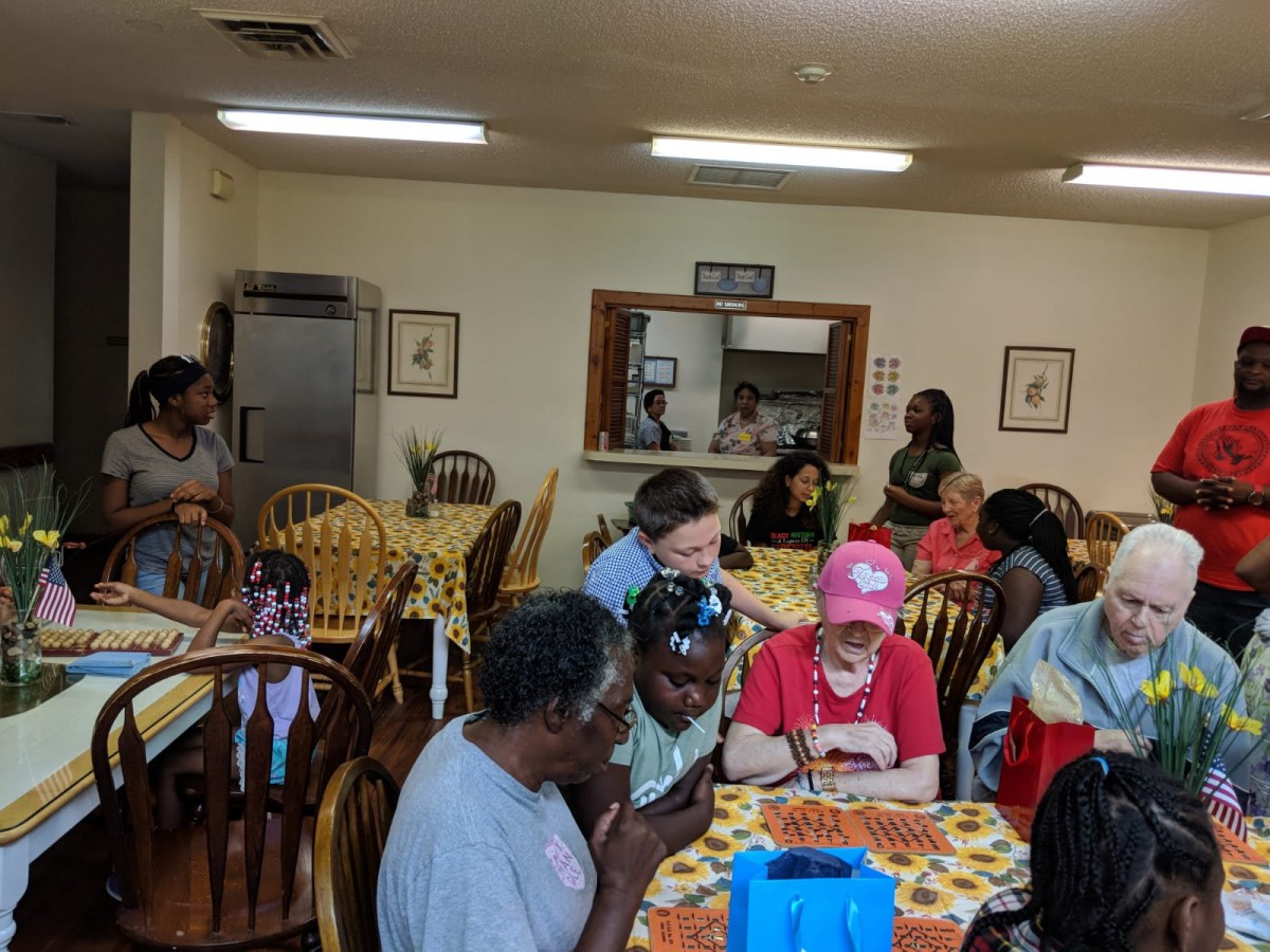 A community gathering with people socializing around tables indoors.