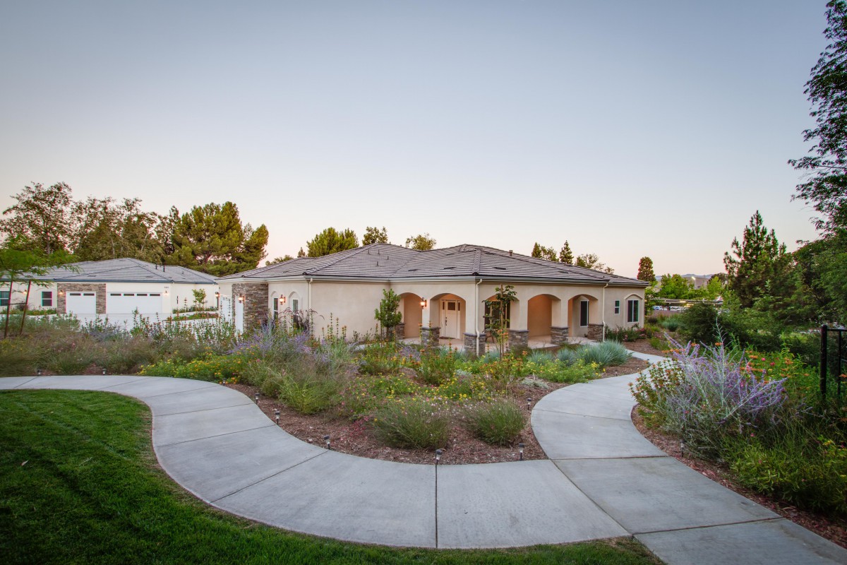 A beautifully landscaped house with a winding driveway at sunset.