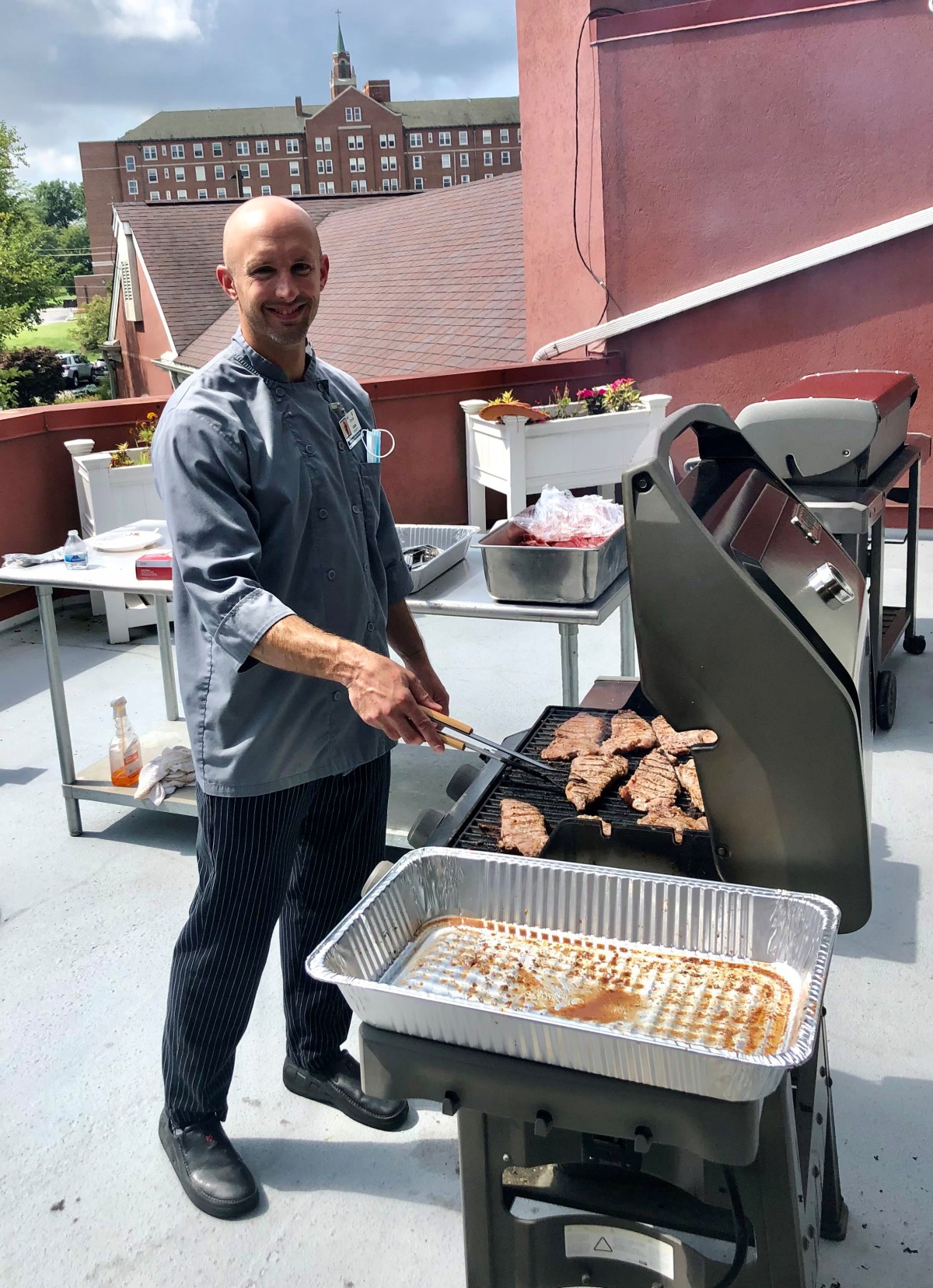 A chef grilling meat on a barbecue in an outdoor setting.