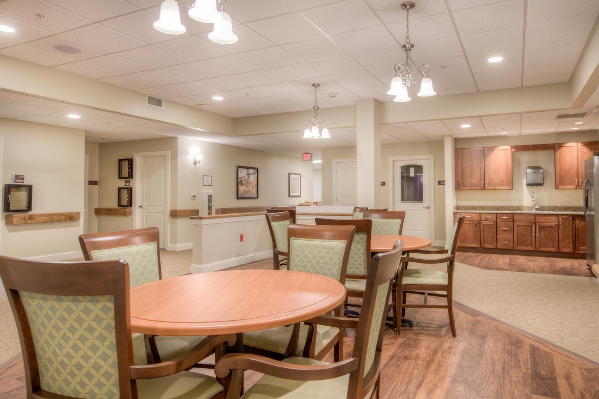 A cozy dining area with wooden tables and cushioned chairs, illuminated by ceiling lights.