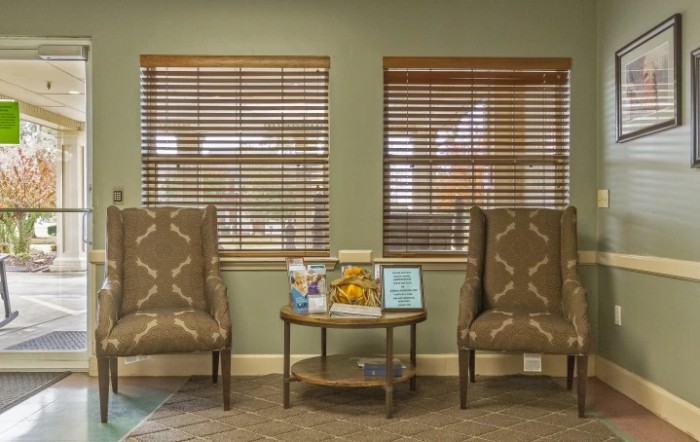 A cozy waiting room with two chairs and a small table between them, featuring window blinds.