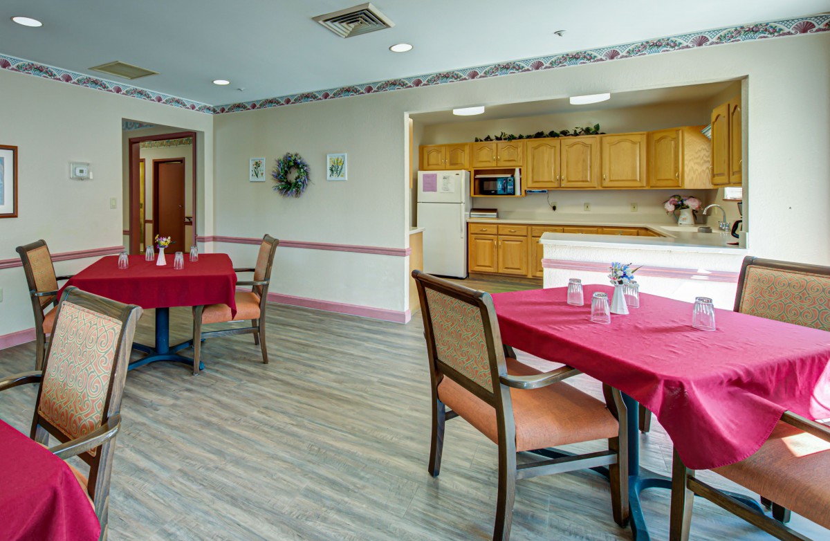 A cozy dining area with red tablecloths and a kitchen in the background.