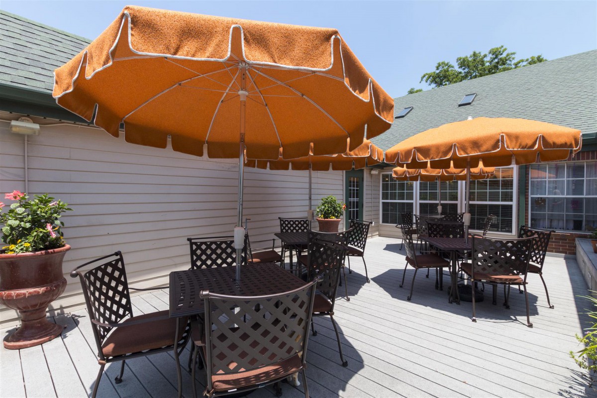 An outdoor patio with tables and chairs shaded by orange umbrellas on a sunny day.