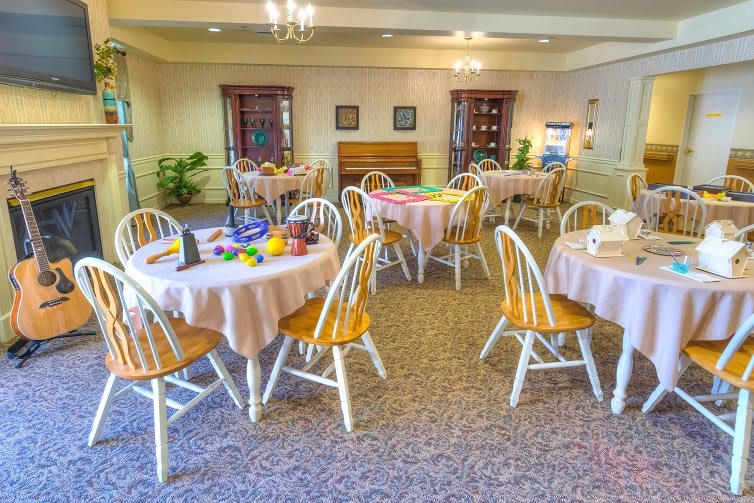 A well-lit dining room with round tables and wooden chairs set for a meal.