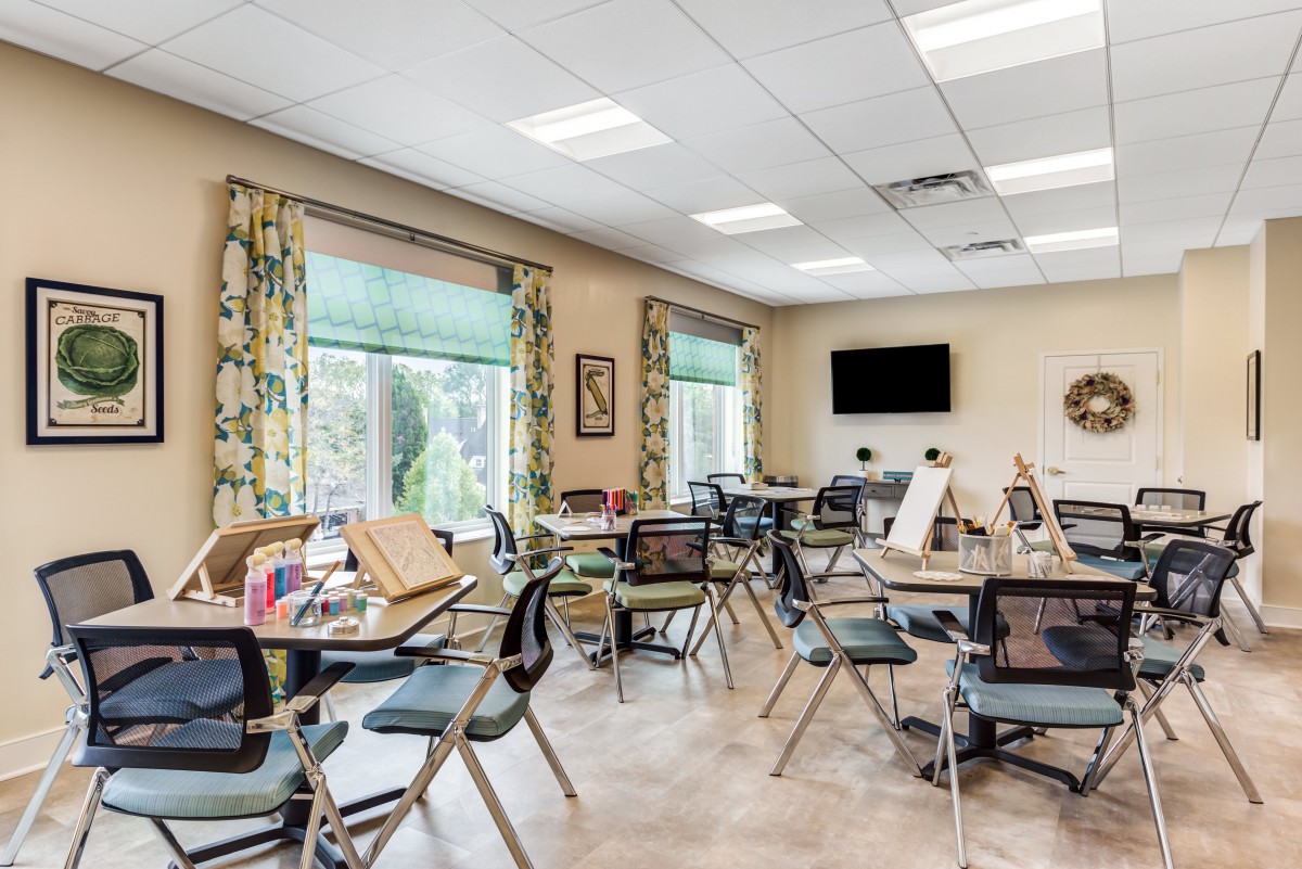 A well-lit classroom with tables and chairs, showcasing art supplies and a television on the wall.