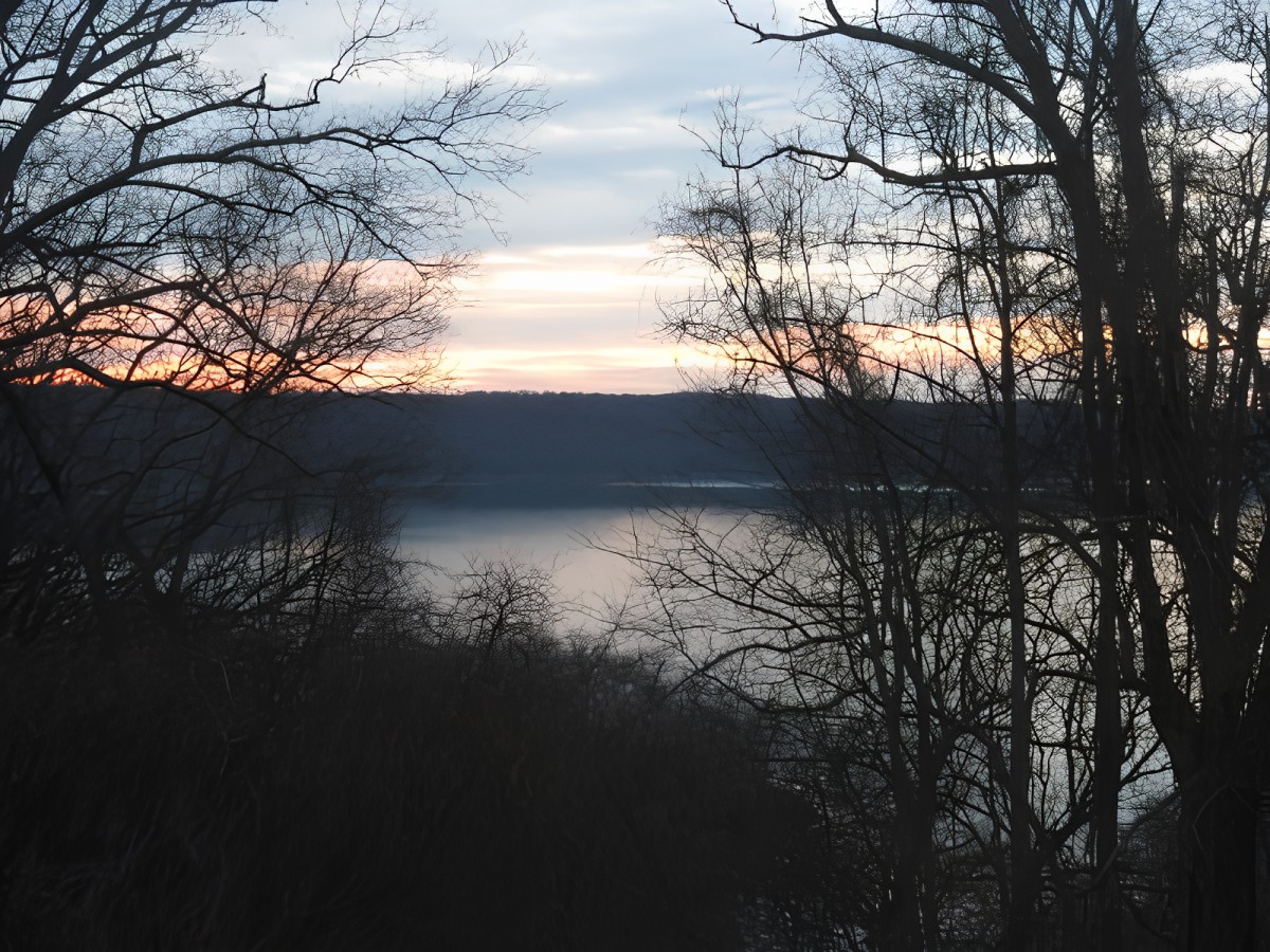 A tranquil view of a lake at sunset, framed by silhouetted trees.