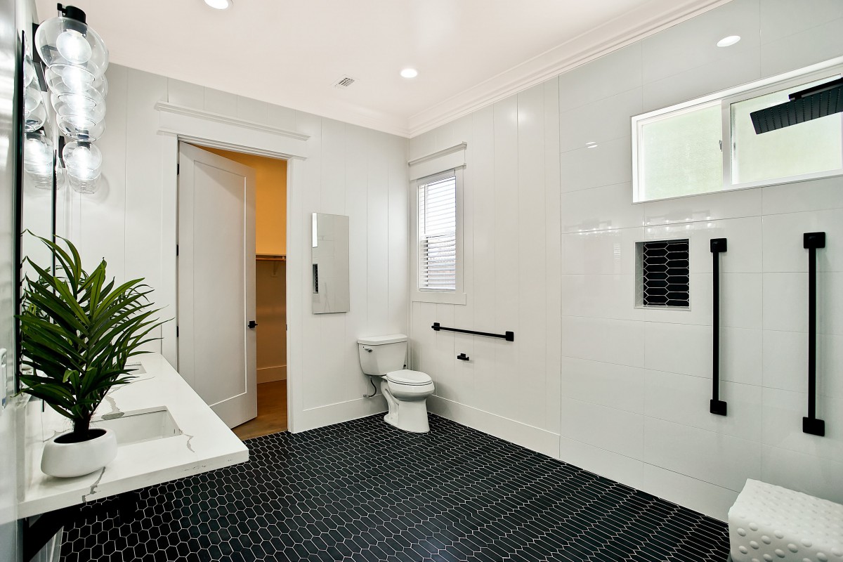 A modern bathroom with sleek white walls and dark floor tiles, featuring a toilet, sink, and mirror.