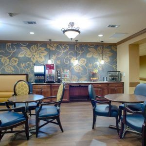 A cozy dining area with multiple tables and chairs, featuring a decorative wallpaper and a beverage station.