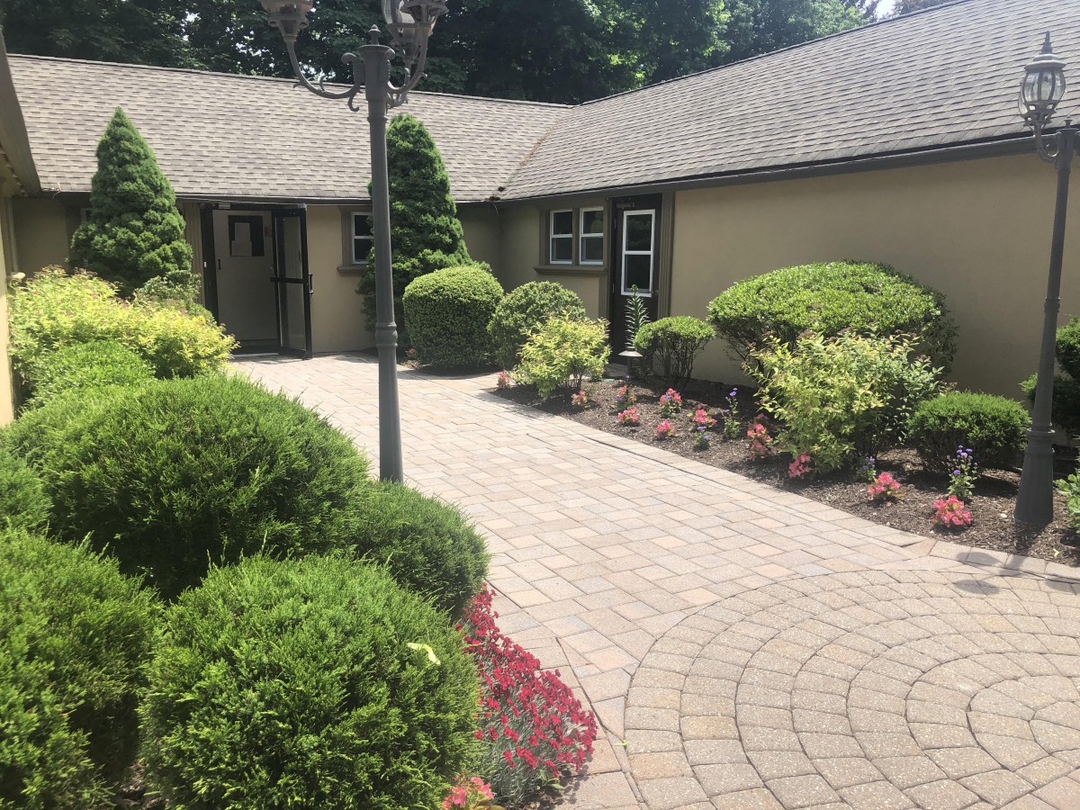 A beautifully landscaped house exterior with a paved pathway and neatly trimmed bushes.