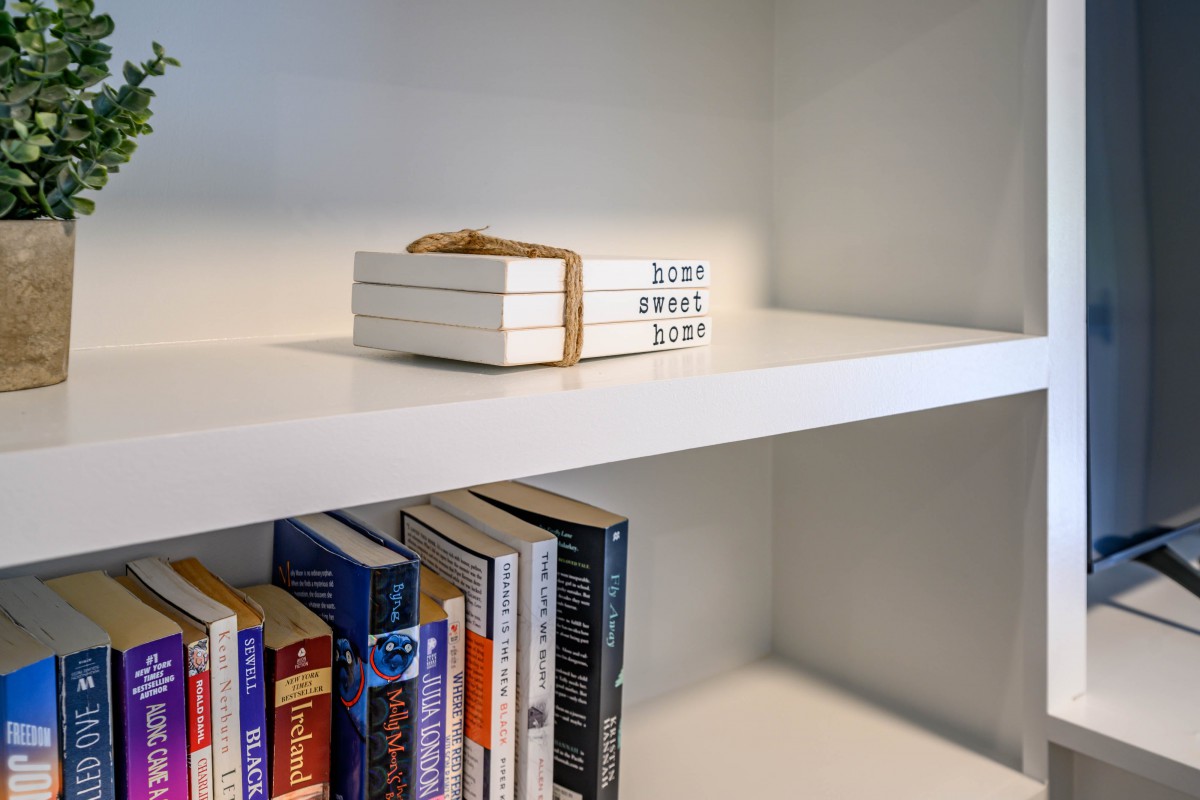 A neatly organized bookshelf with a stack of books tied together on the top shelf.