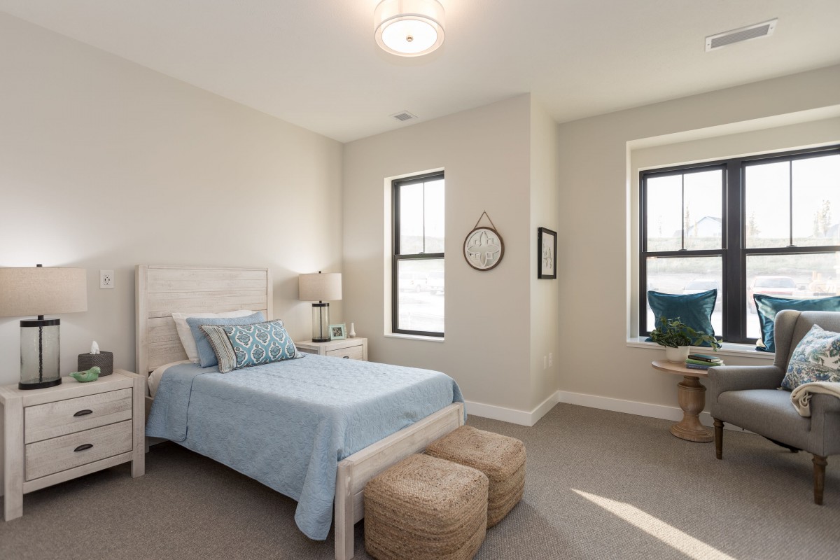 A modern and minimalist bedroom featuring a bed with blue linens, natural lighting, and neutral tones.