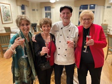 A group of people, including a chef, celebrating with glasses of champagne indoors.