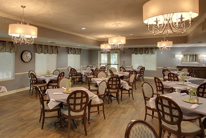 An elegant dining room with neatly arranged tables and chairs, featuring chandeliers for ambient lighting.