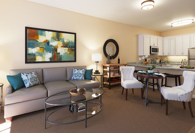 A modern living room featuring a comfortable sofa, glass coffee table, abstract artwork, and a small dining area connected to the kitchen.