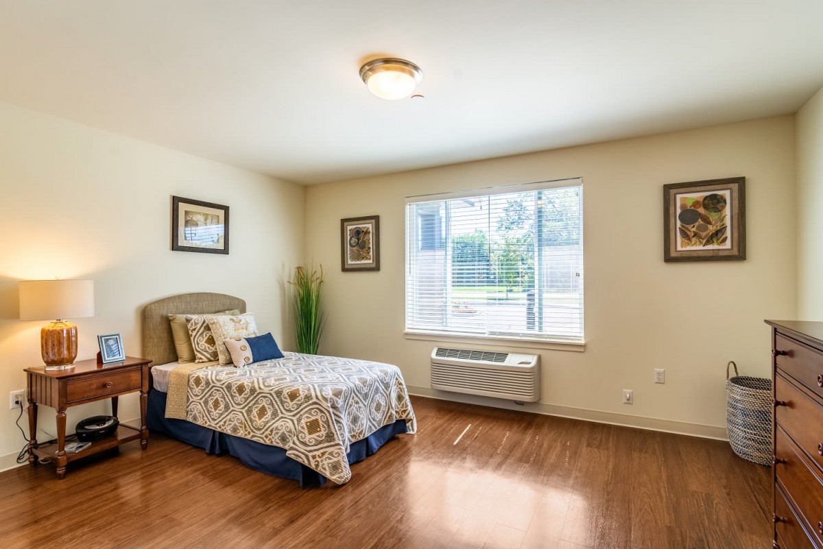 A cozy bedroom with a single bed, hardwood floors, and a large window allowing natural light.