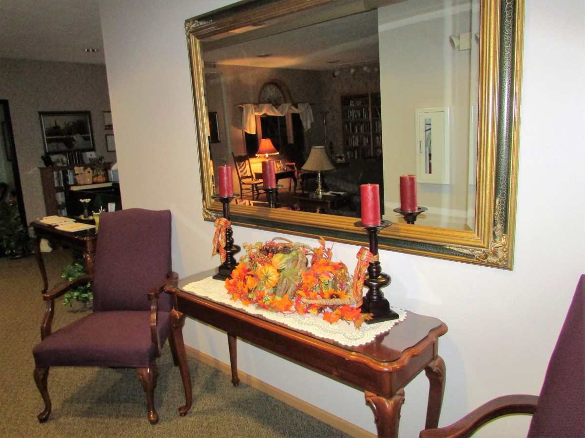 A decorated console table with autumn-themed arrangements and candle holders in a warmly lit room with a mirror above.