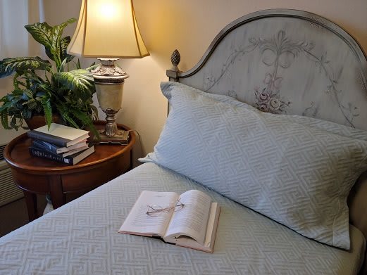 A cozy bedroom with a book open on the bed and a lamp illuminating the room.