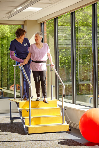 A healthcare professional assists an elderly patient during a physical therapy session on a stair apparatus.
