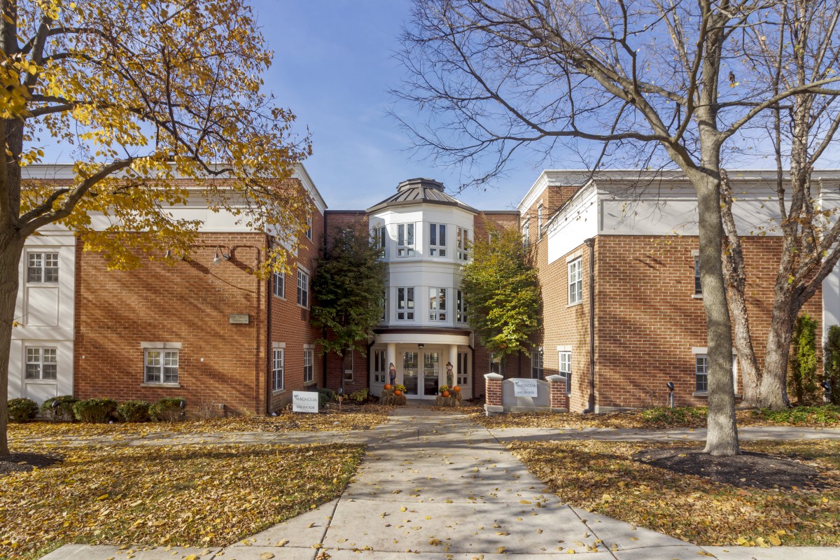 A brick building with an entrance surrounded by autumn trees and a pathway leading up to it.