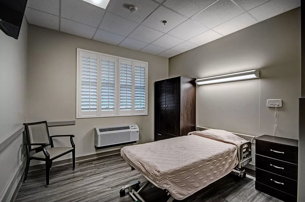 A clean and minimalist hospital room with a single bed and simple furnishings.