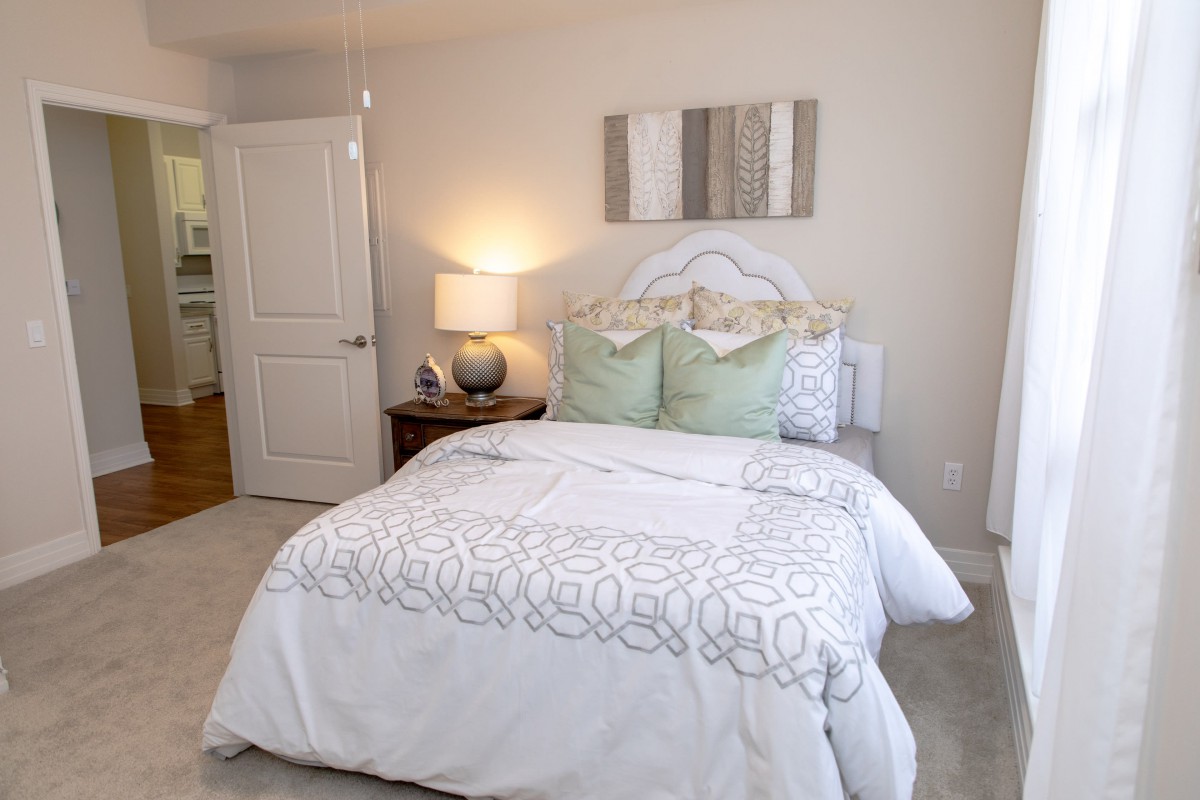 A cozy bedroom with a neatly made bed, decorative pillows, a nightstand, and a lamp.