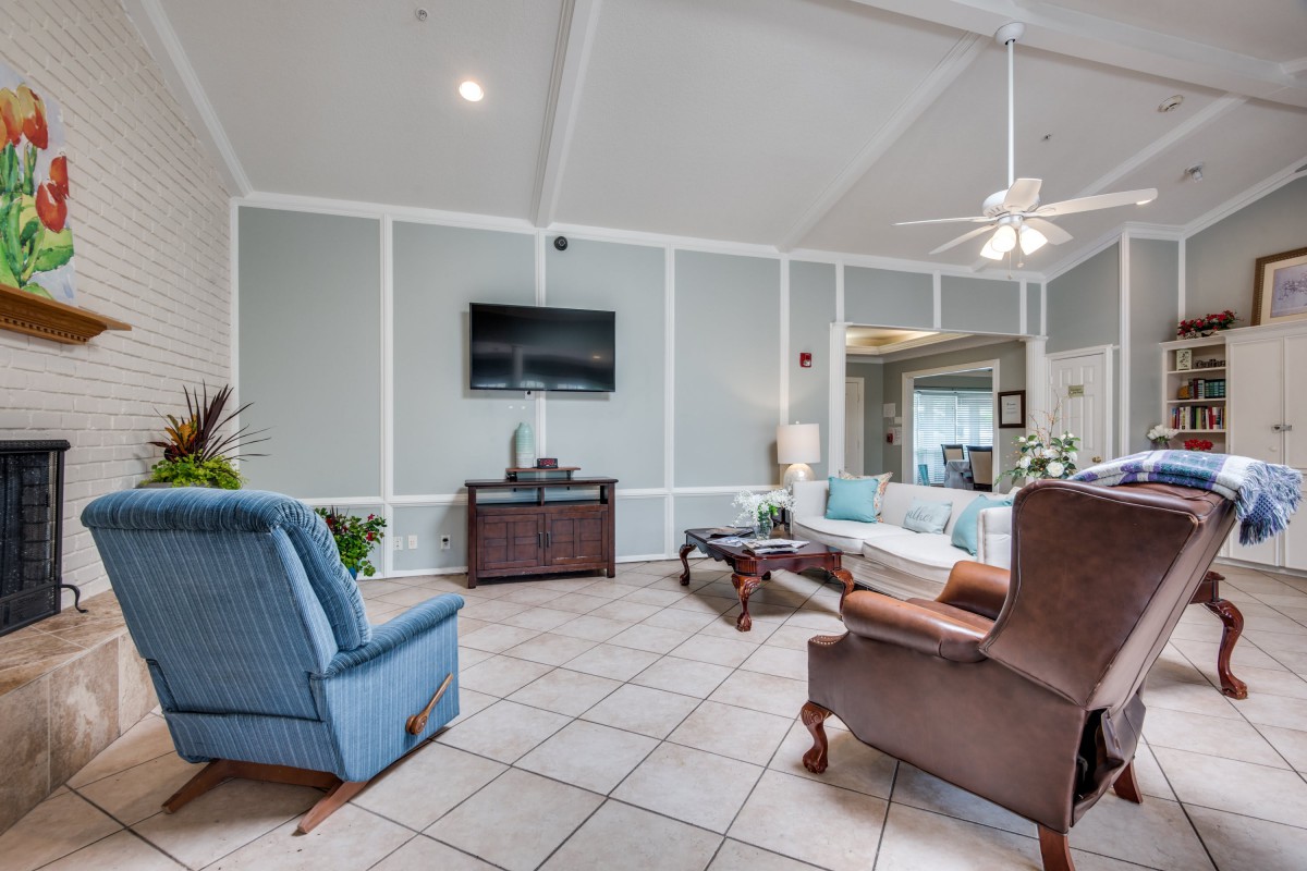 A spacious living room featuring comfortable seating, a wall-mounted television, and a ceiling fan.
