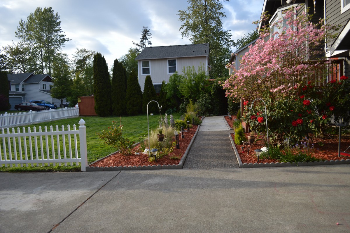 A beautifully landscaped garden with a pathway leading to a house, surrounded by flowers and greenery.