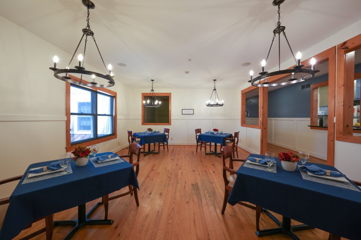 A cozy dining area with blue tablecloths, wooden floors, and elegant chandeliers.