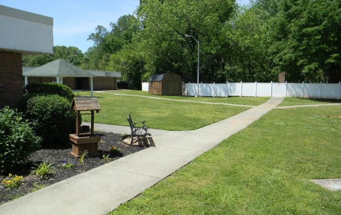 A well-maintained garden area with a concrete pathway, bench, and decorative well.