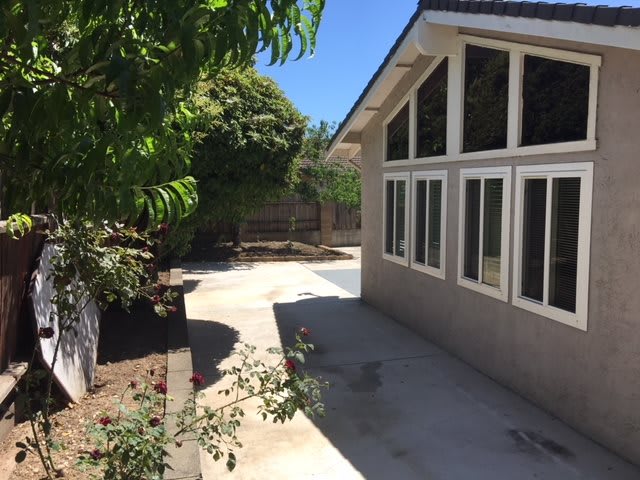 A sunny backyard patio beside a house with large windows and surrounding greenery.